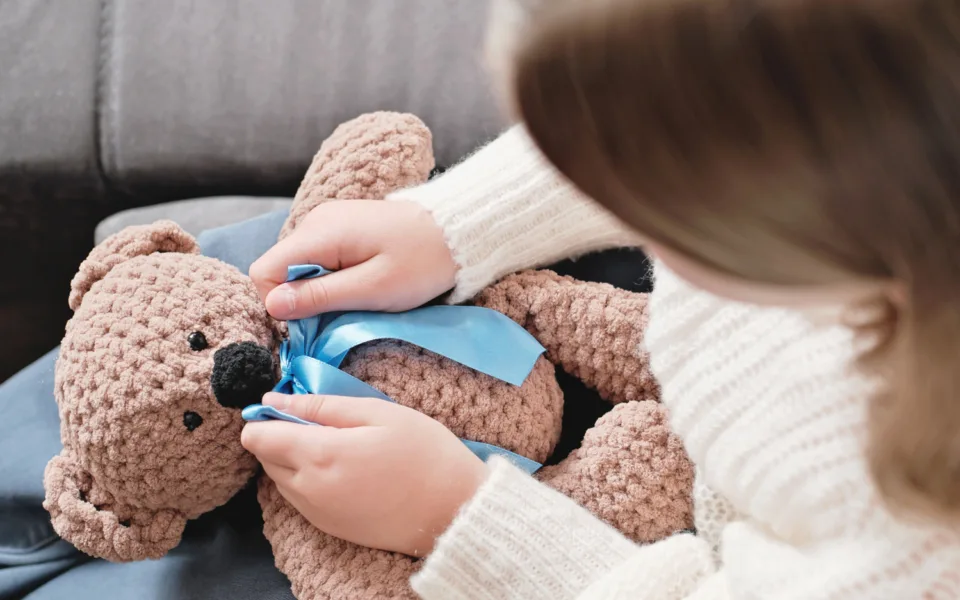 Mp51033728 little girl playing with knitted teddy bear and ties a